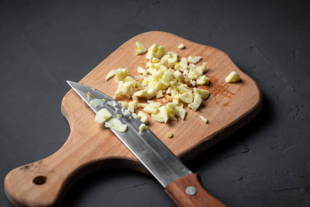 Finely chopped garlic on a wooden board with a knife on a gray background.