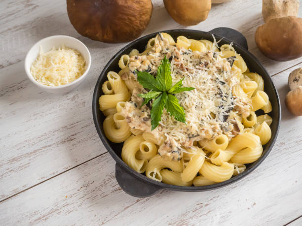 Pasta with penny bun on a cast iron pan on a white wooden table