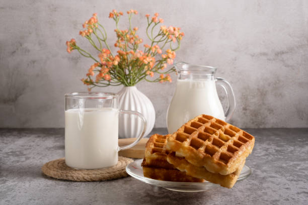 Sweet breakfast of Belgian waffles and a glass of milk on a grey background.