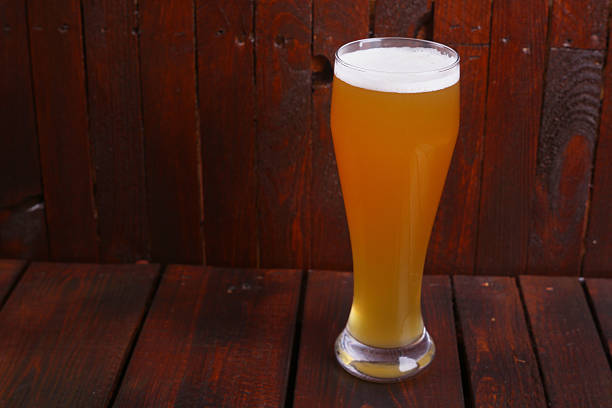 A tall glass full of light wheat beer standing on a wooden table